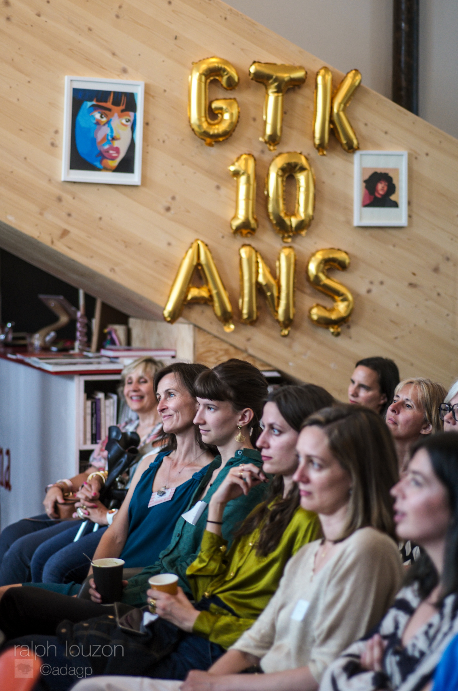 Au premier plan, les personnes assises au premier rang de la plénière, à l'arrière plan, les ballons GTK 10 ans accrochés au mur