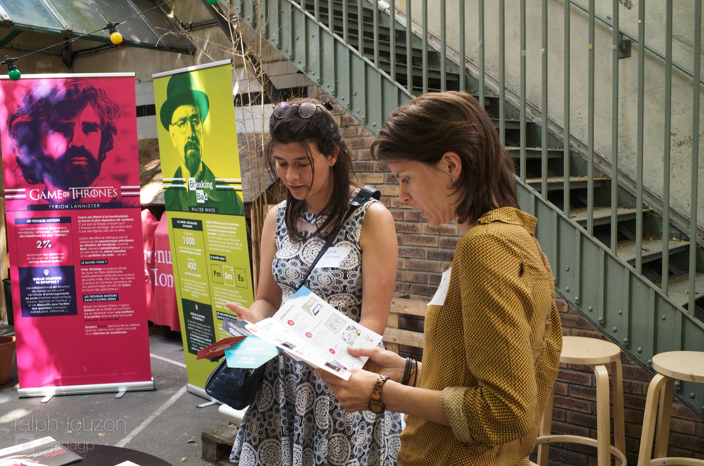 Au premier plan, 2 personnes regardent les goodies GTK, en arrière plan l'expo Séries et Handicap